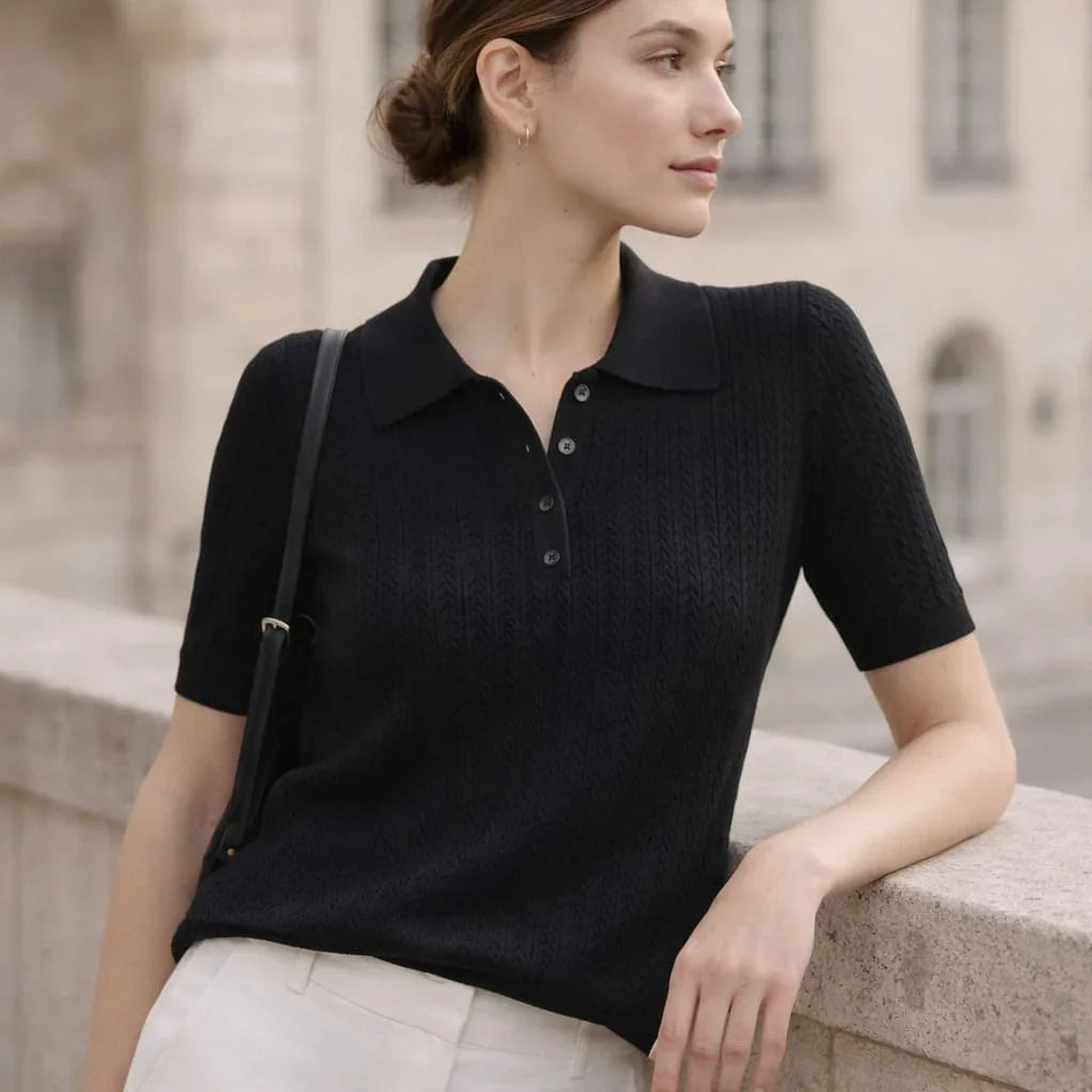 Woman wearing a black short sleeve knit polo shirt with buttons, leaning on a stone ledge outdoors