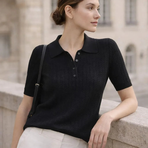 Woman wearing a black short sleeve knit polo shirt with buttons, leaning on a stone ledge outdoors