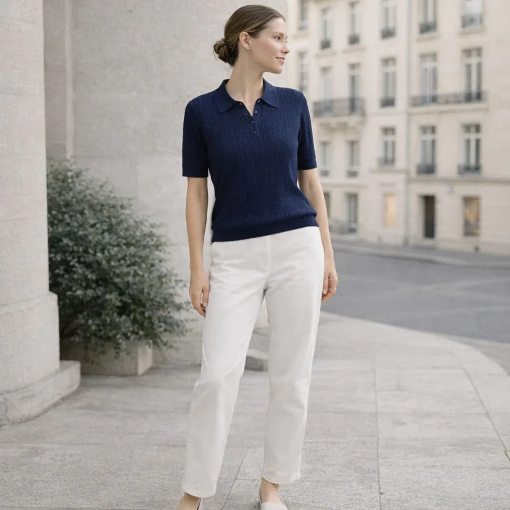 Woman wearing navy knit polo shirt and white pants standing outdoors in an urban setting