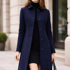 Woman wearing a navy long coat with large buttons, black dress, urban background