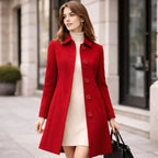 Woman wearing a red long coat over a cream turtleneck dress on a city street