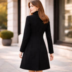 Woman in a tailored black long coat standing outdoors on a city street