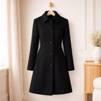Elegant black long coat with button closure, tailored fit, hanging in a modern interior.