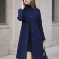 Woman wearing a navy blue long coat with large buttons, standing outdoors