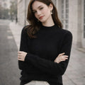 Woman wearing a black high-neck jumper and pearl earrings standing outdoors