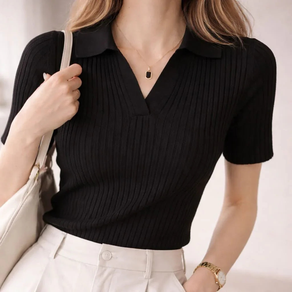 Woman wearing a black ribbed knit polo shirt with short sleeves and light high-waisted trousers.