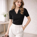 Woman wearing a black ribbed polo shirt and white high-waisted trousers indoors