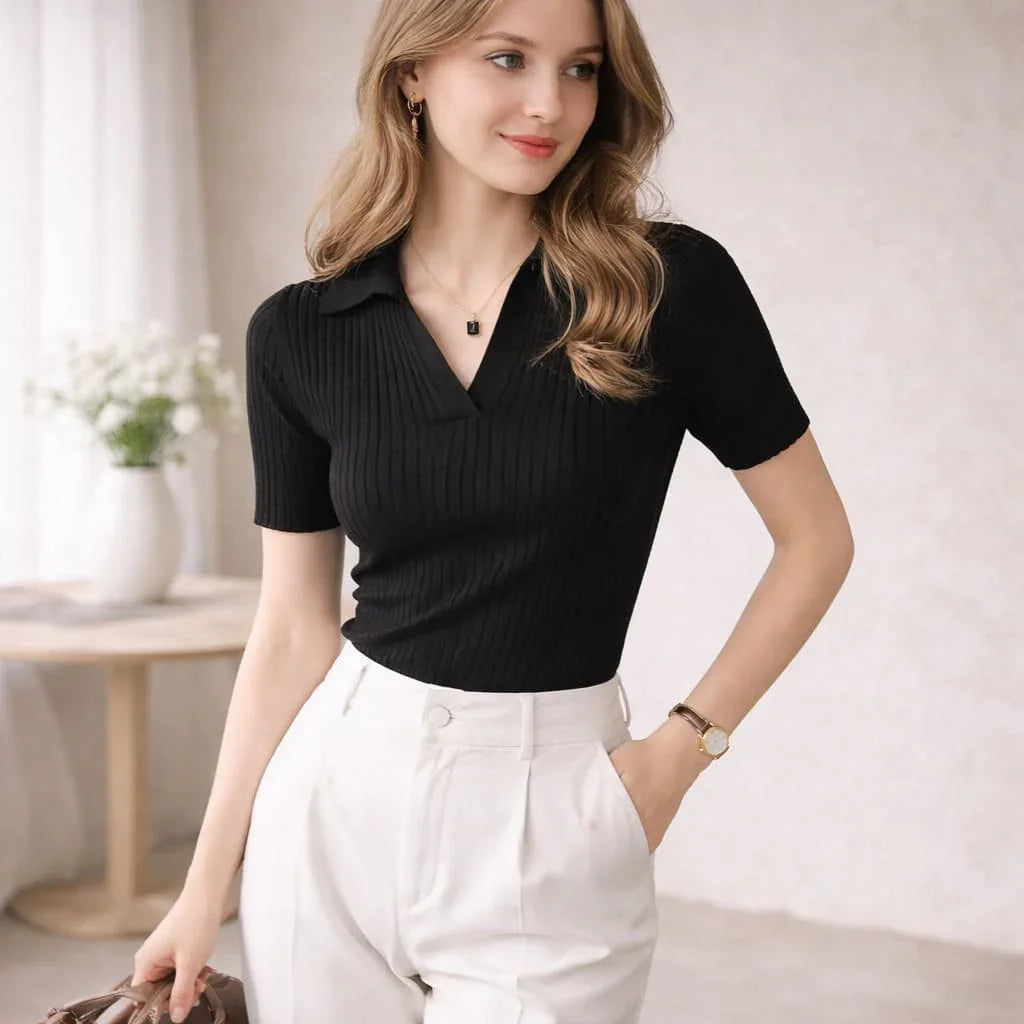 Woman wearing a black ribbed polo shirt and white high-waisted trousers indoors