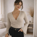 Woman wearing beige ribbed flared sleeve blouse with V-neck in modern bedroom.