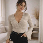Woman wearing beige ribbed flared sleeve blouse with V-neck in modern bedroom.