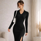 Woman wearing a black ribbed knit V-neck long sleeve dress with a side slit, holding a white bag.